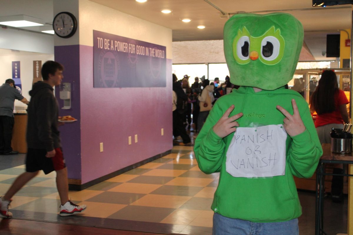 A student dressed as the Duolingo owl with a Spanish or Vanish sign adds humor to the Halloween festivities.