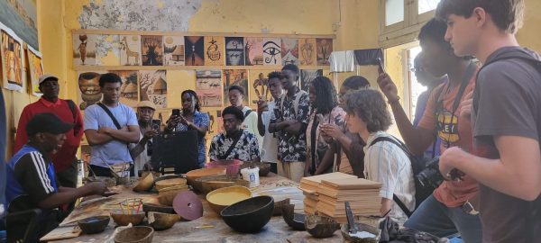 Students attentively listen as a local artisan in Senegal teaches them about traditional Senegalese craft-making techniques during a workshop.