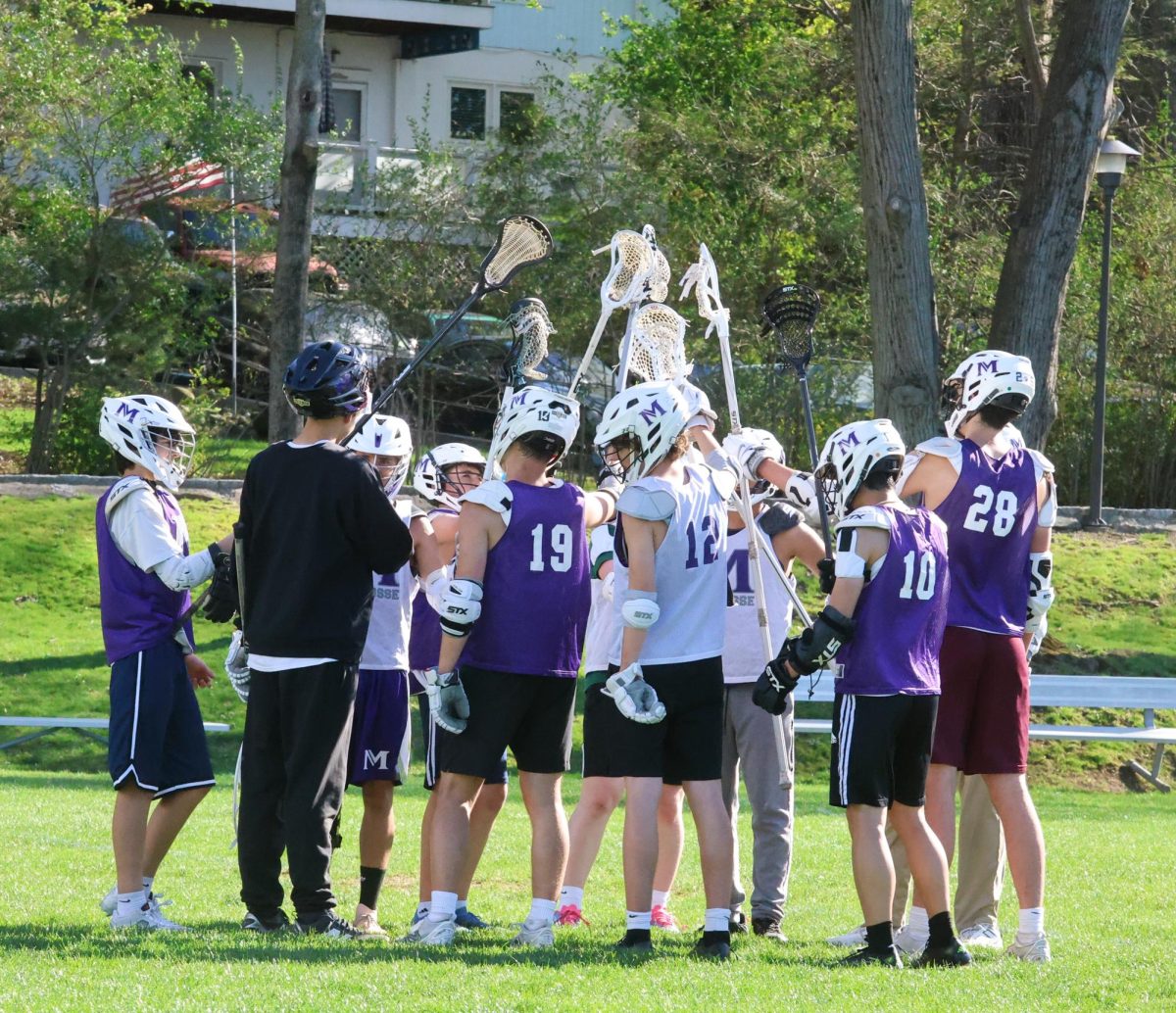 The varsity boys lacrosse team huddles during their practice on West Field. They lift their sticks to the air—ready to bring more intensity to their practice. They aim to have a successful season this year under new coaching