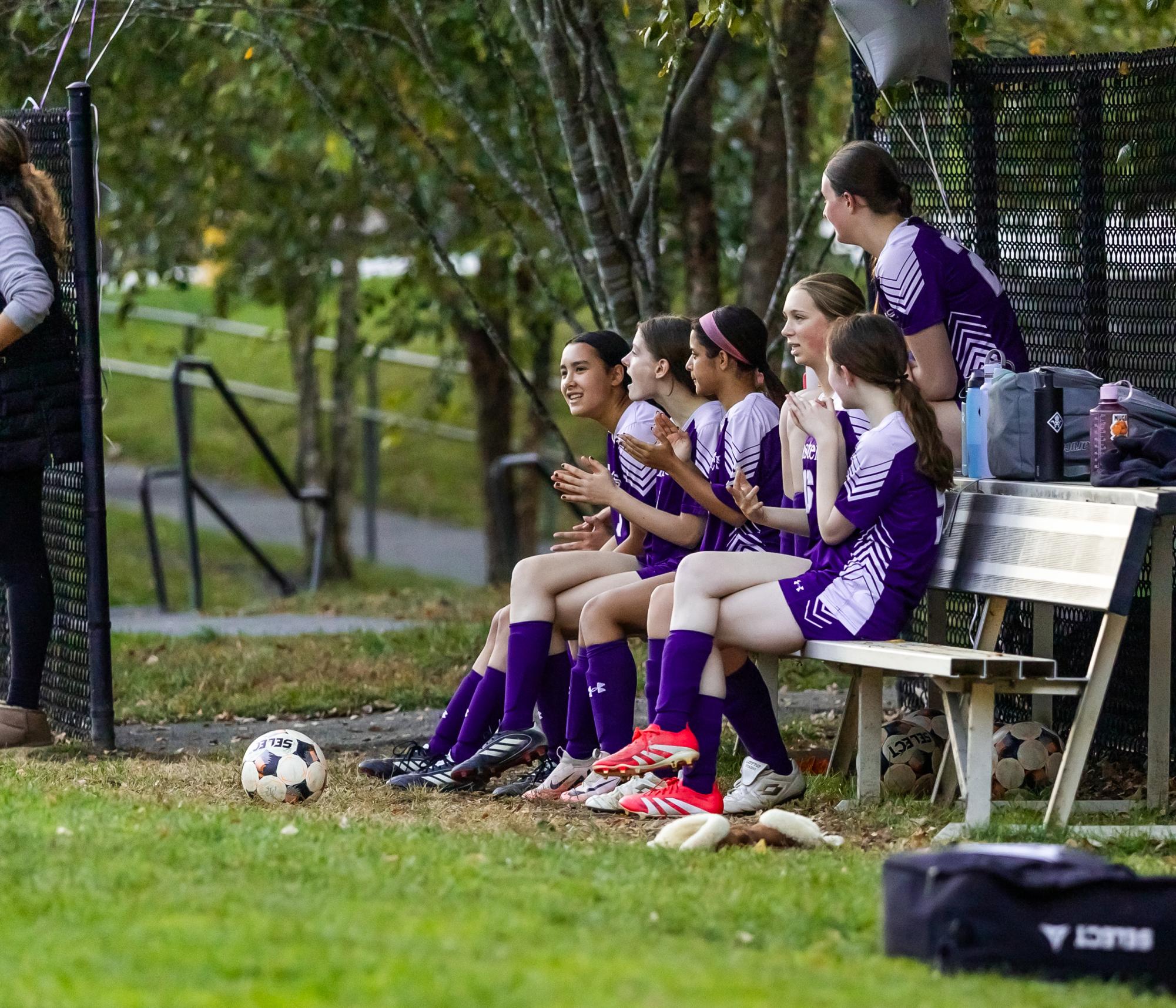 The girls Junior varsity team sitting on a bench cheering for their teammates.